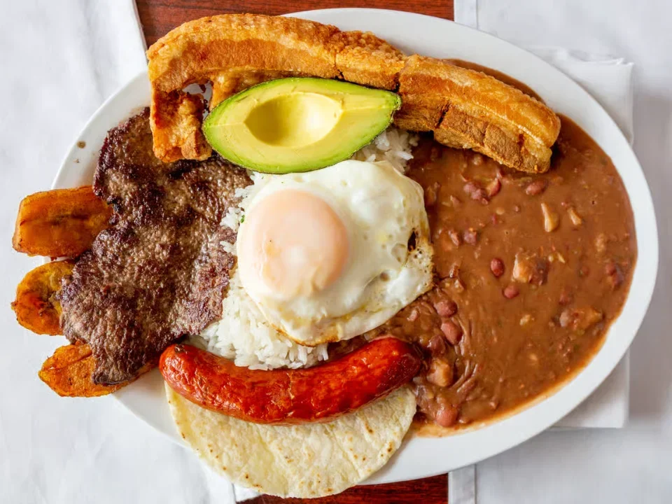 Bandeja Paisa (Paisa Platter) - The ultimate Colombian platter with steak, pork belly, chorizo, rice, beans, egg, avocado, and arepa.